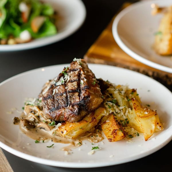 Grilled steak with mushroom sauce, roasted potatoes, and parmesan cheese on a white plate.