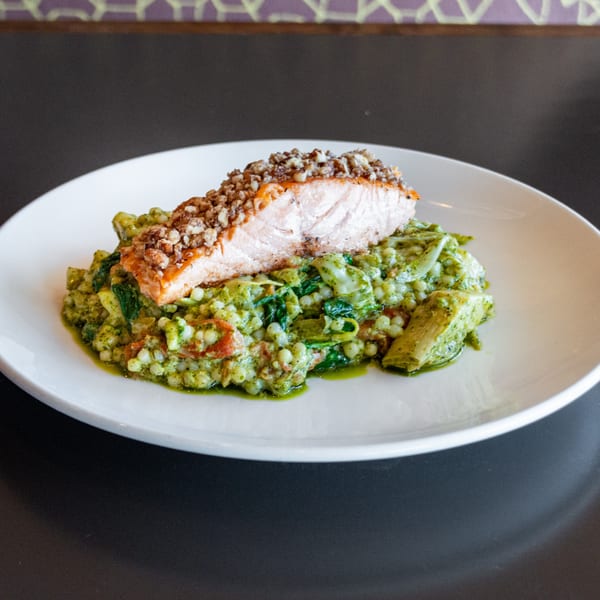 A salmon fillet with a nut crust on a bed of green pesto couscous with spinach and tomatoes.