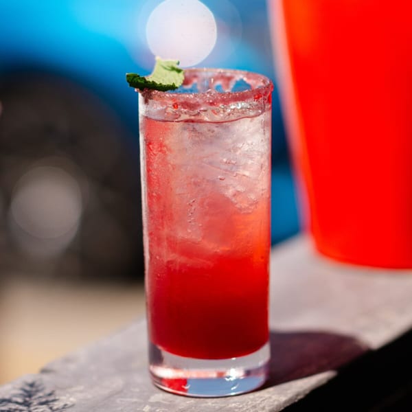 A vibrant red cocktail with ice, a sugar-rimmed glass, and a mint garnish.