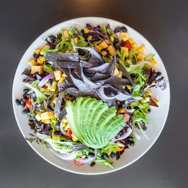 Overhead view of a vibrant Ripe Eatery salad with avocado, black beans, corn, cheese, and tortilla strips.