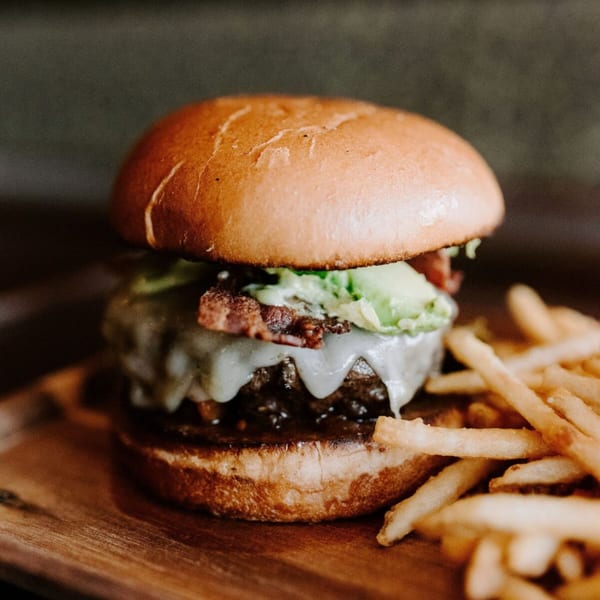 A Ripe Eatery burger with melted cheese, bacon, and avocado, served with golden fries.