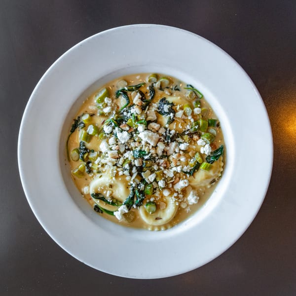 Overhead view of ravioli in a creamy sauce with spinach, asparagus, and crumbled feta cheese.