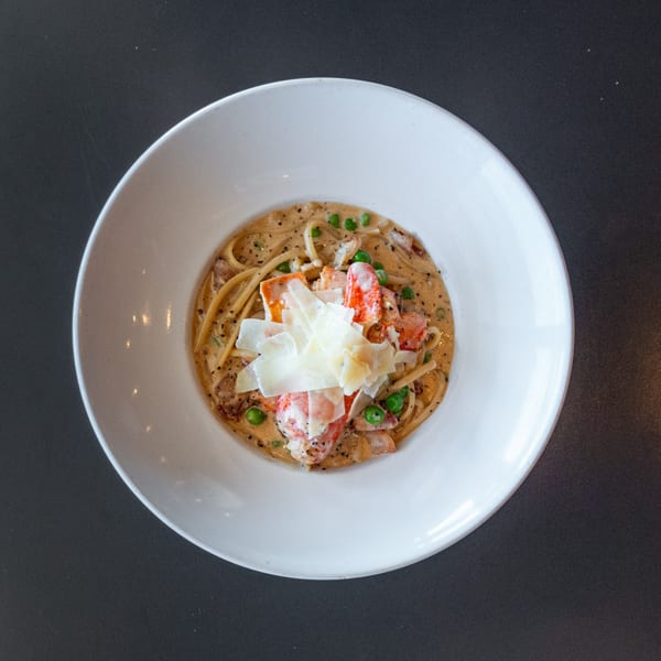 Overhead view of Ripe Eatery's lobster pasta with peas and shaved parmesan in a white bowl.