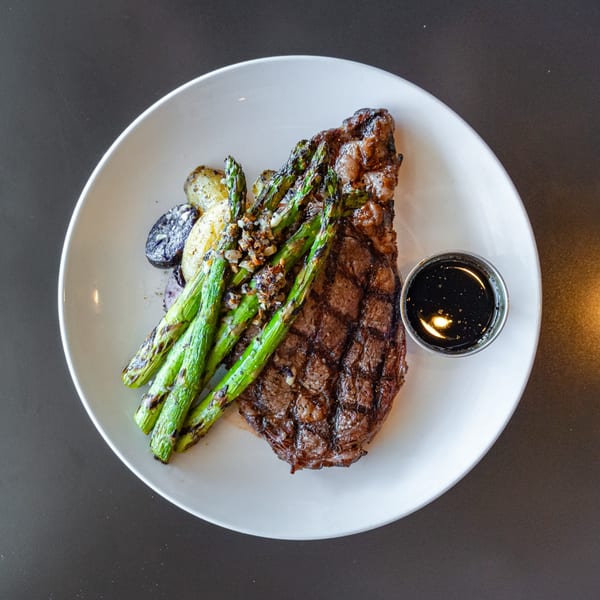 Grilled steak with asparagus, roasted potatoes, and a side of dark sauce on a white plate.