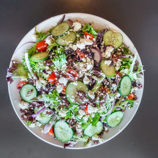 A vibrant Ripe Eatery salad with mixed greens, cucumbers, tomatoes, red onion, olives, and feta cheese.