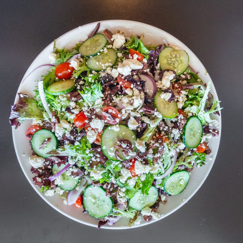 A vibrant Ripe Eatery salad with mixed greens, cucumbers, tomatoes, red onion, olives, and feta cheese.