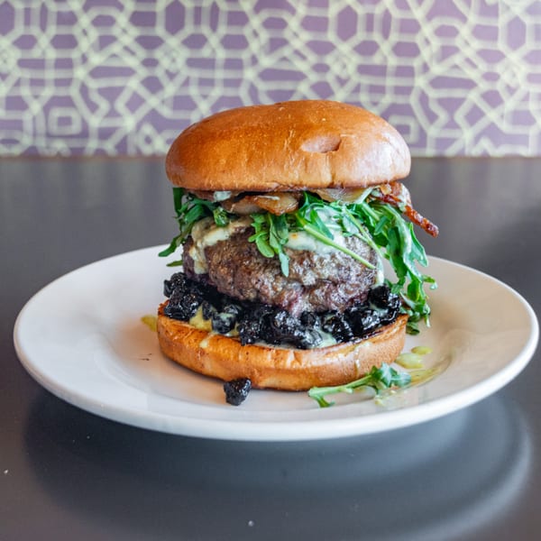 Gourmet burger with arugula, melted cheese, caramelized onions, and dark berry compote on a bun.