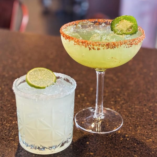 Two margaritas, one with a lime slice and salt rim, the other with a jalapeño and chili rim.