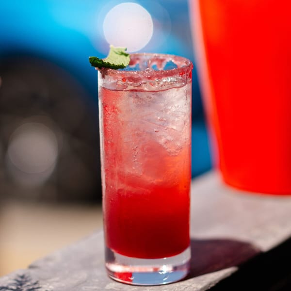 A vibrant red cocktail with ice, a sugar-rimmed glass, and a mint garnish.