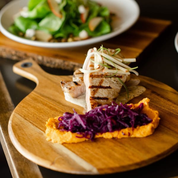 Grilled pork chops with mashed sweet potatoes and red cabbage, with a salad in the background.