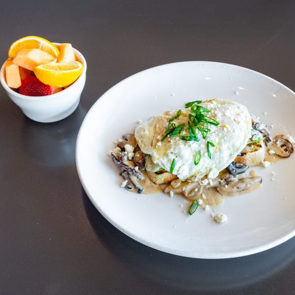 A Ripe Eatery dish with poached eggs, mushrooms, and sauce, served with a side of fruit.