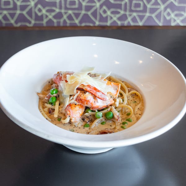 Creamy lobster pasta with peas and shaved parmesan in a white bowl at Ripe Eatery.